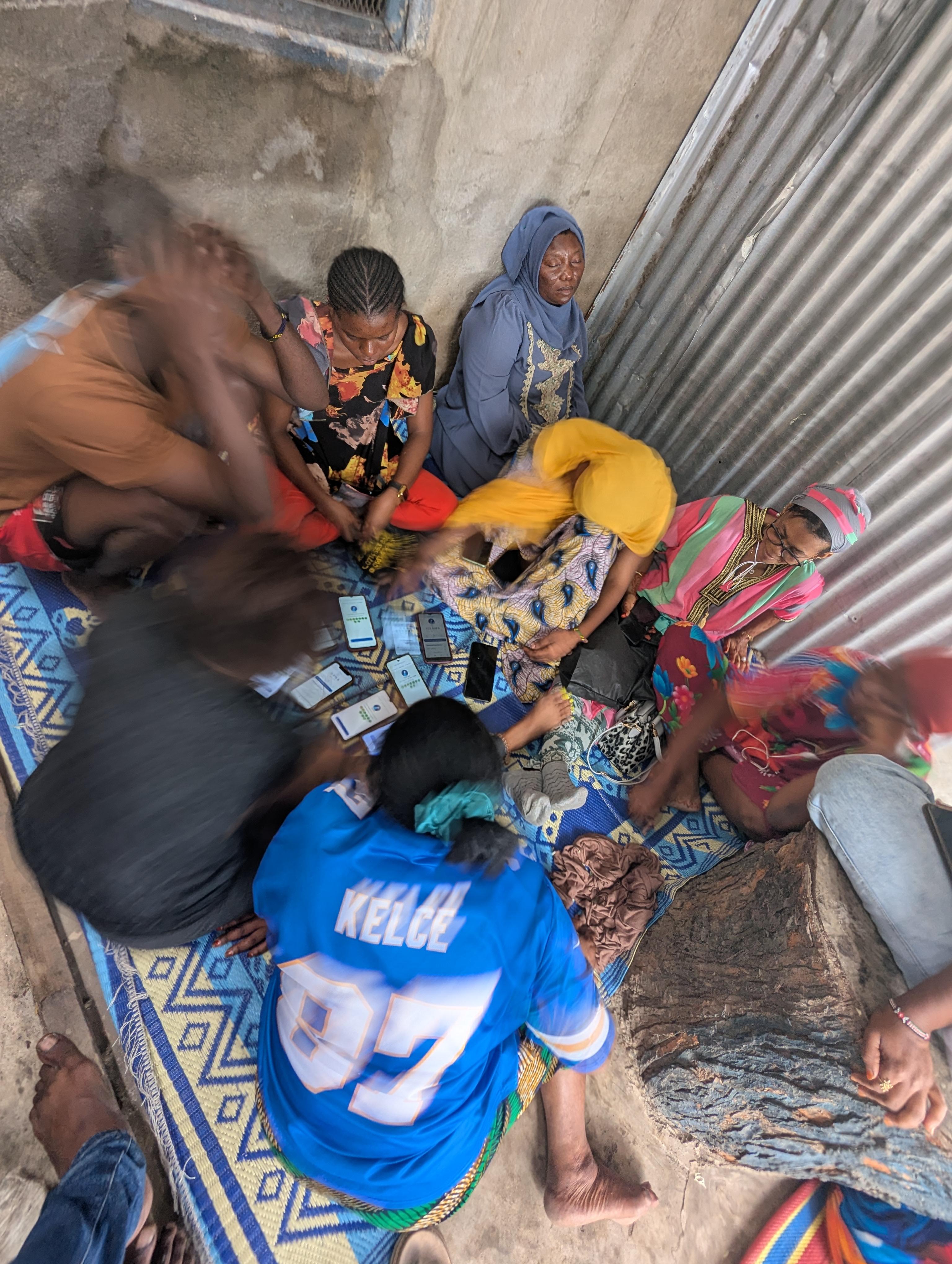 A savings group meeting in Dar es Salaam, members recording contributions on their phones
